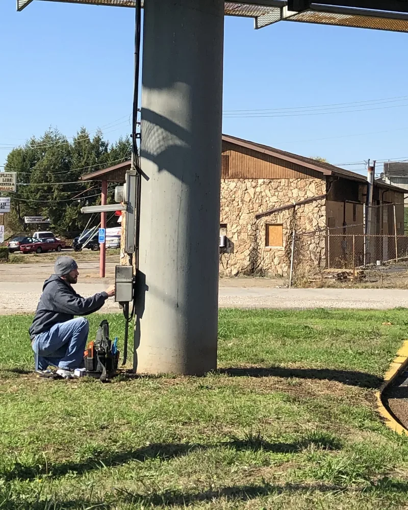 Worker kneeling to wire an electrical box mounted on a billboard support post