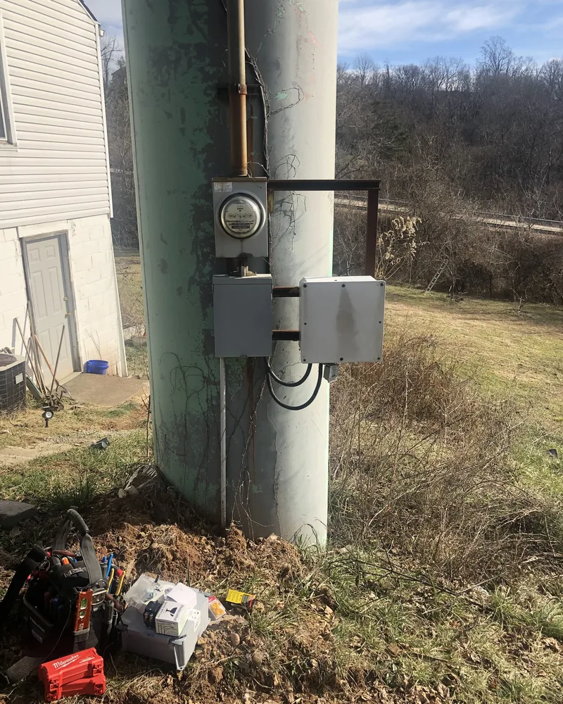 Electric meter and weatherproof boxes mounted on a service pole, with tools on the ground below